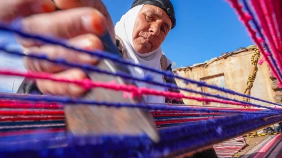 Evinin bahçesindeki tezgahta asırlık yöntemle kilim dokuyor
